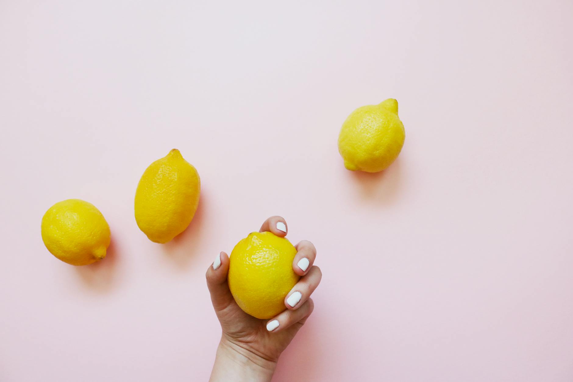 A hand holding a lemon on a soft pink background, symbolizing sensitivity changes