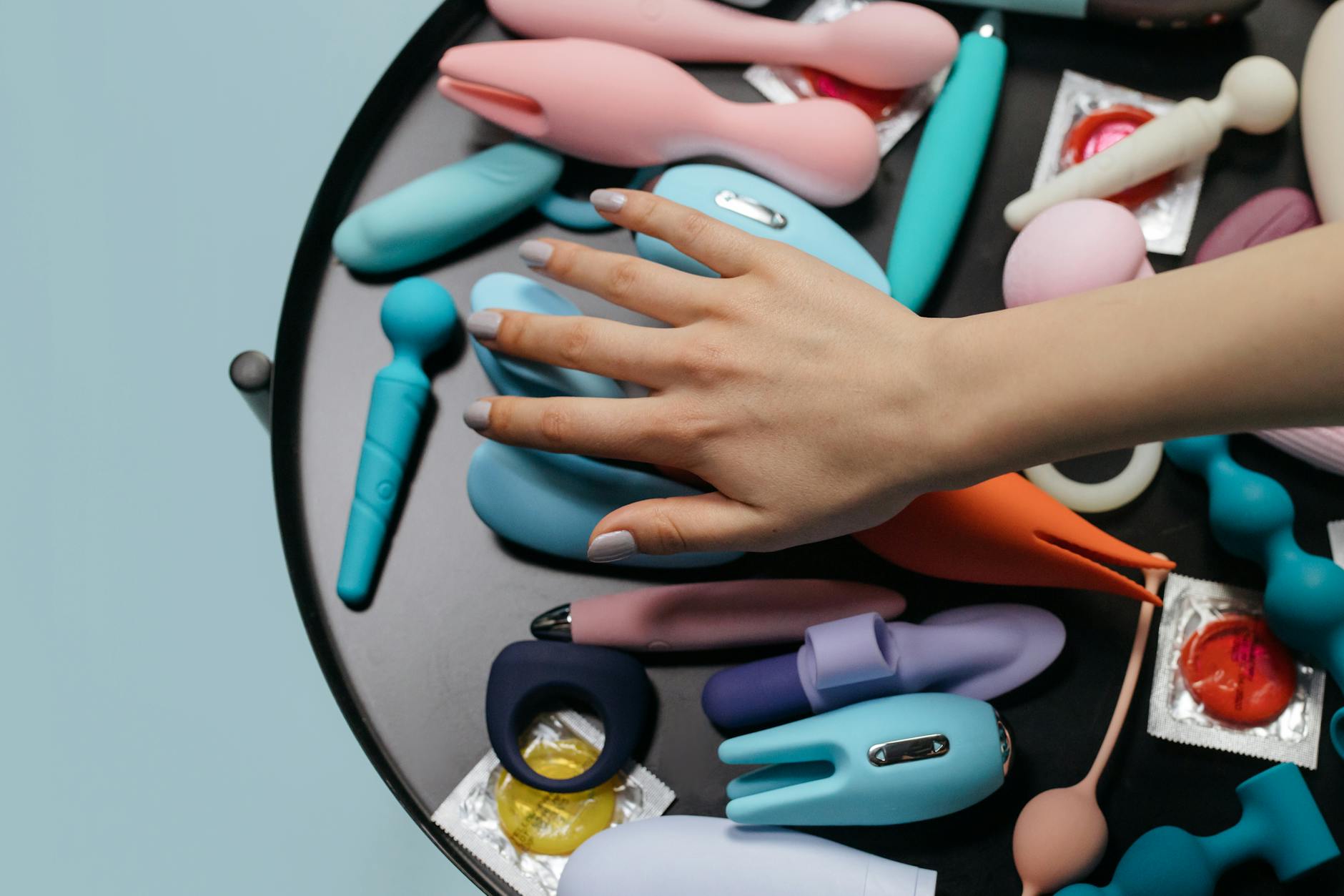 Woman holding a pink vibrator with books in the background, representing intimate self-care during postpartum recovery