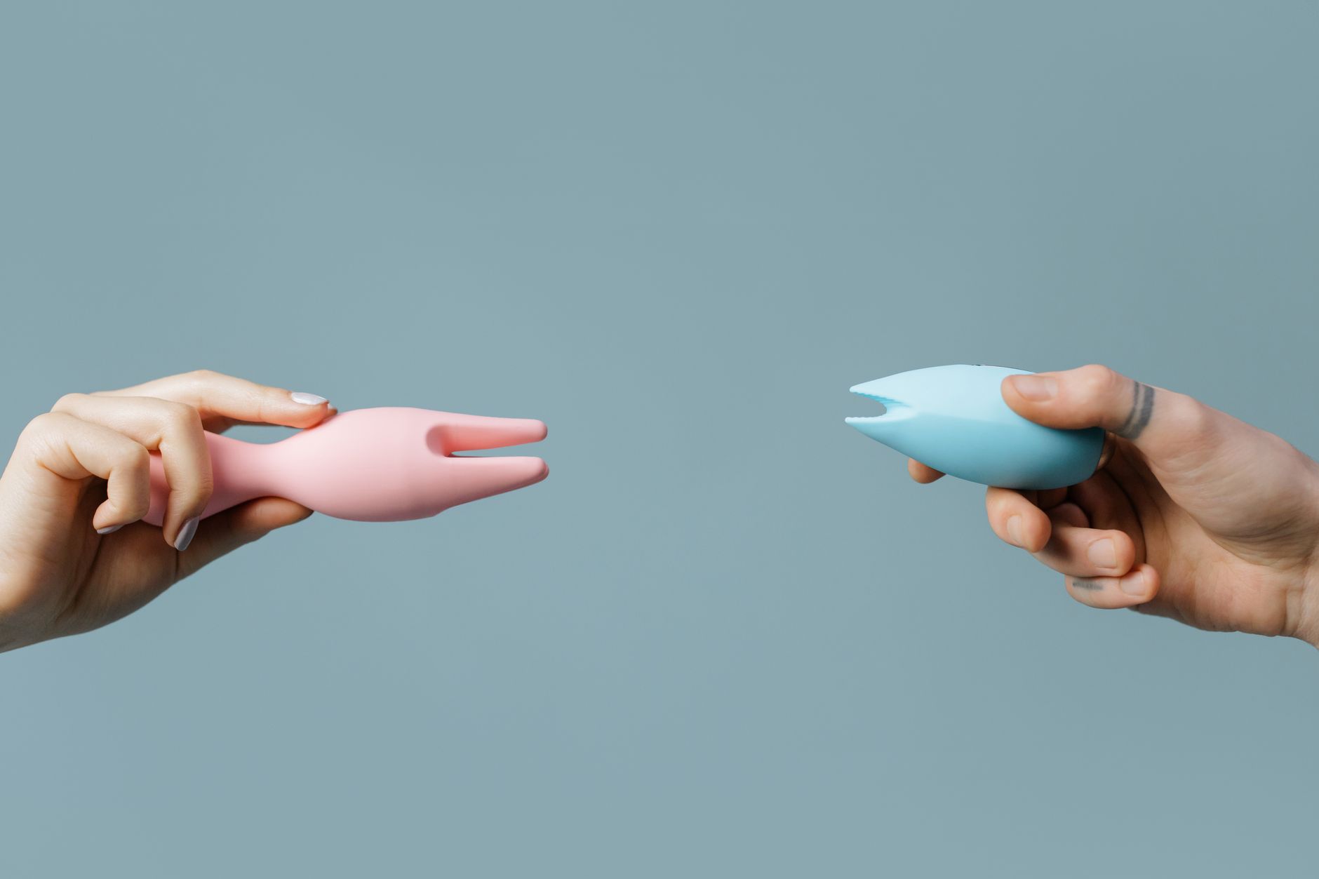 Two hands holding pink and blue silicone vibrators against a pastel background, symbolizing self-care and personal choice
