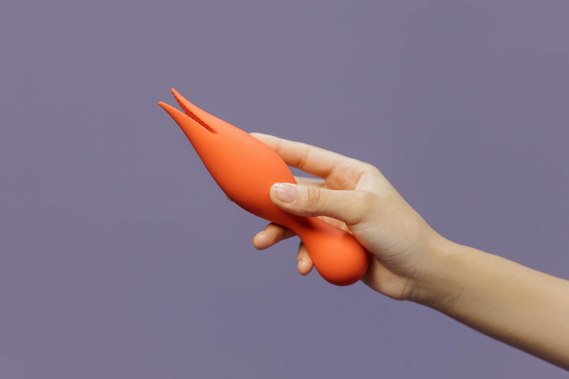 Close-up of a hand holding an orange lemon vibrator against a minimalistic purple backdrop, showcasing modern sensuality.
