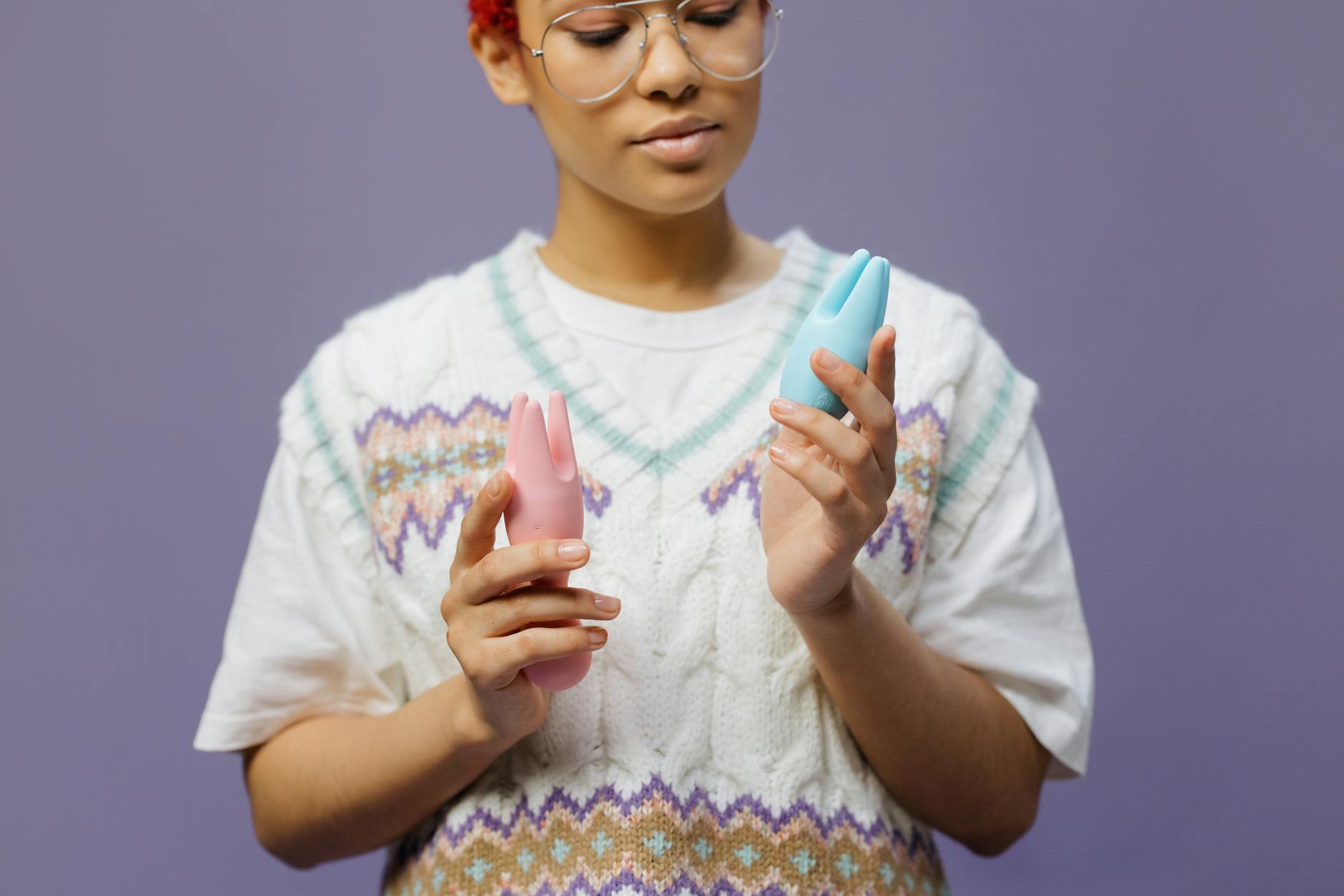 Woman thoughtfully holding colorful vibrators, considering her own pleasure