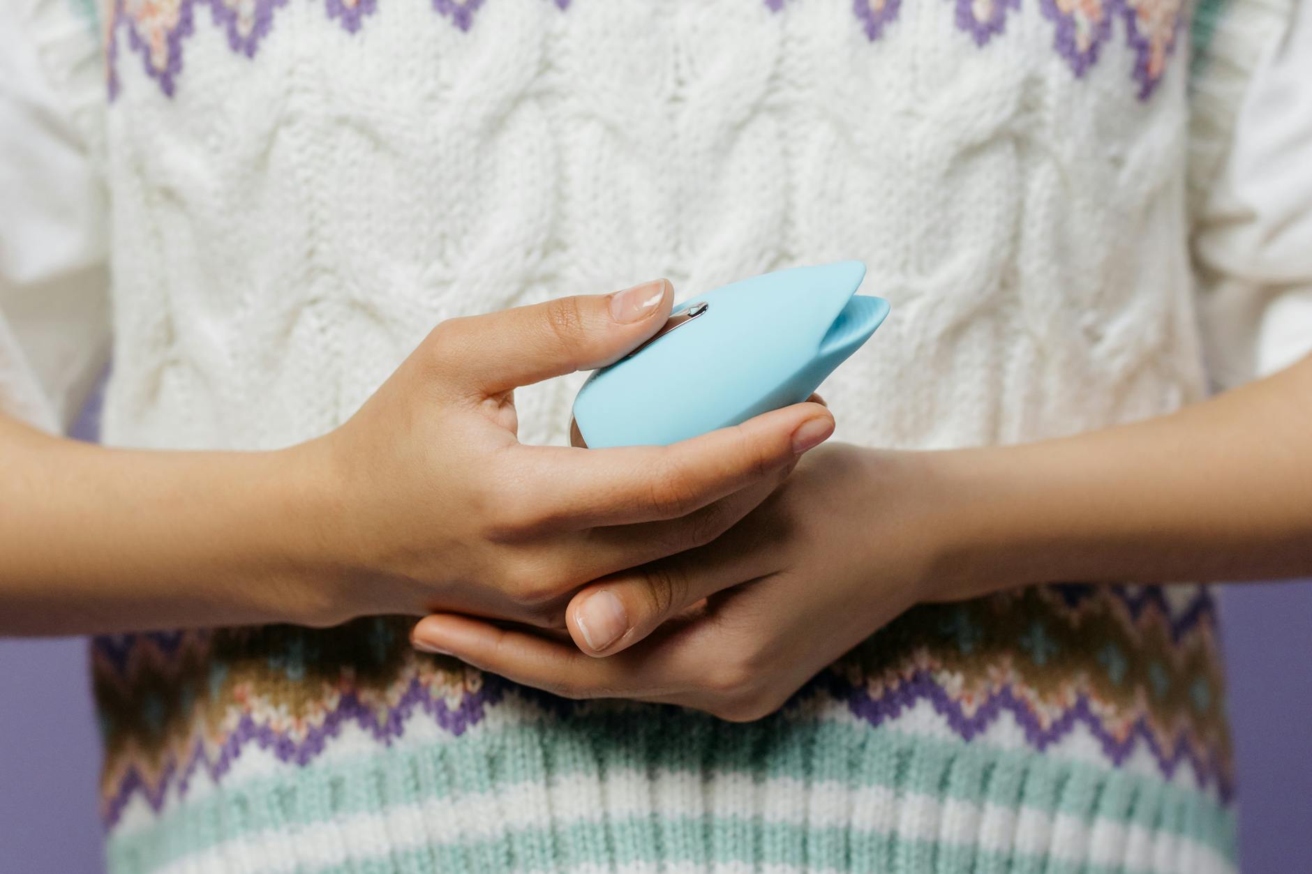 Hands holding a blue lemon clitoral vibrator against a knitted sweater