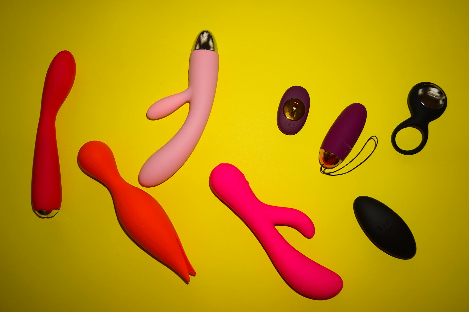 Colorful collection of clitoral vibrators and adult toys displayed on a bright yellow surface