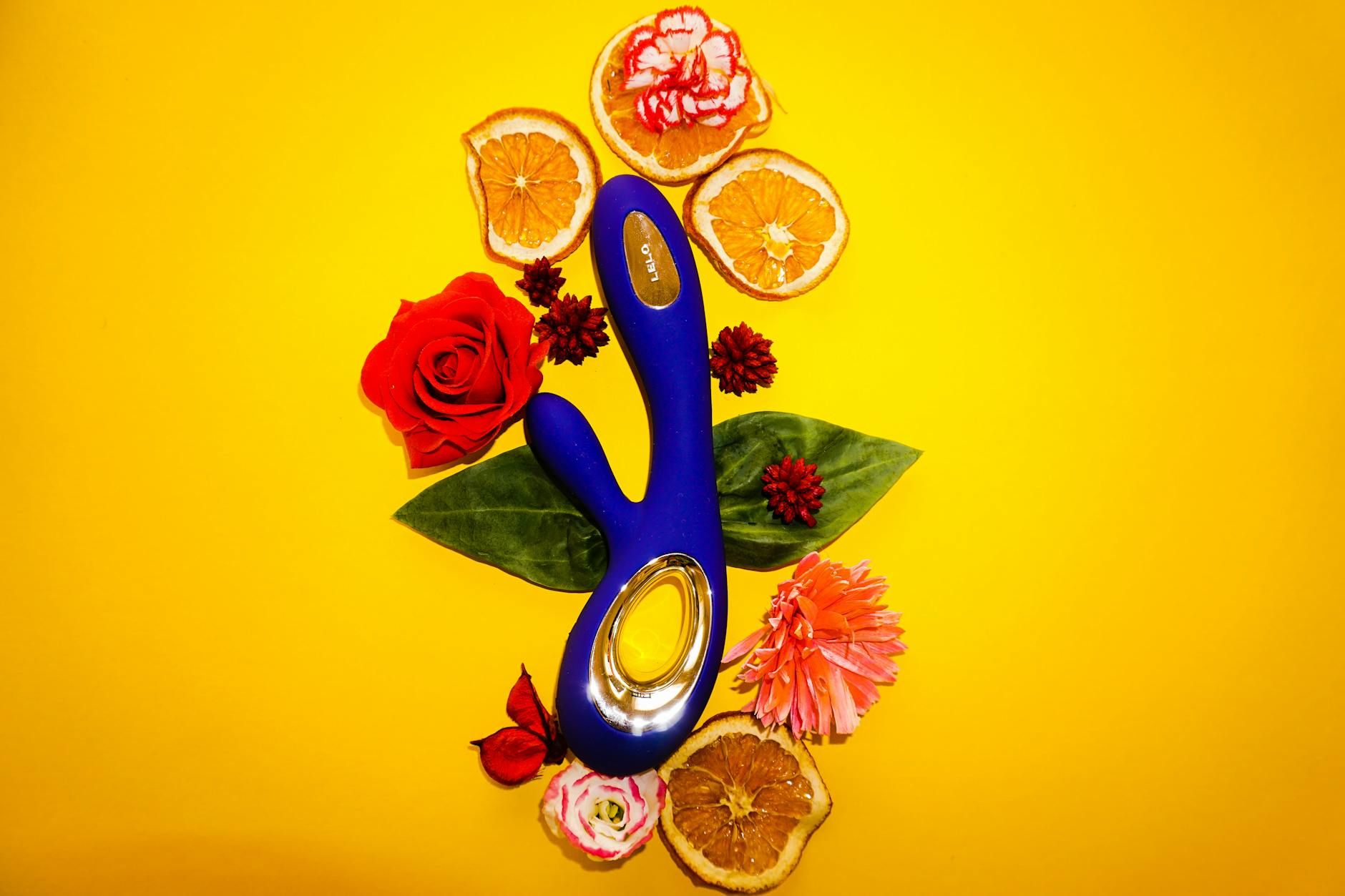 A blue lemon clitoral vibrator surrounded by flowers and citrus slices on a bright yellow background
